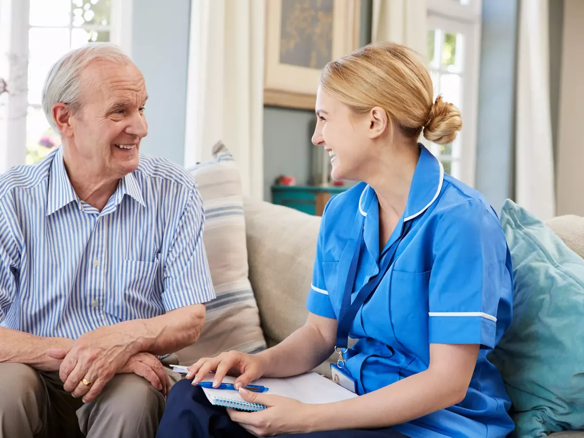 An older man and his carer chatting and laughing together on the sofa