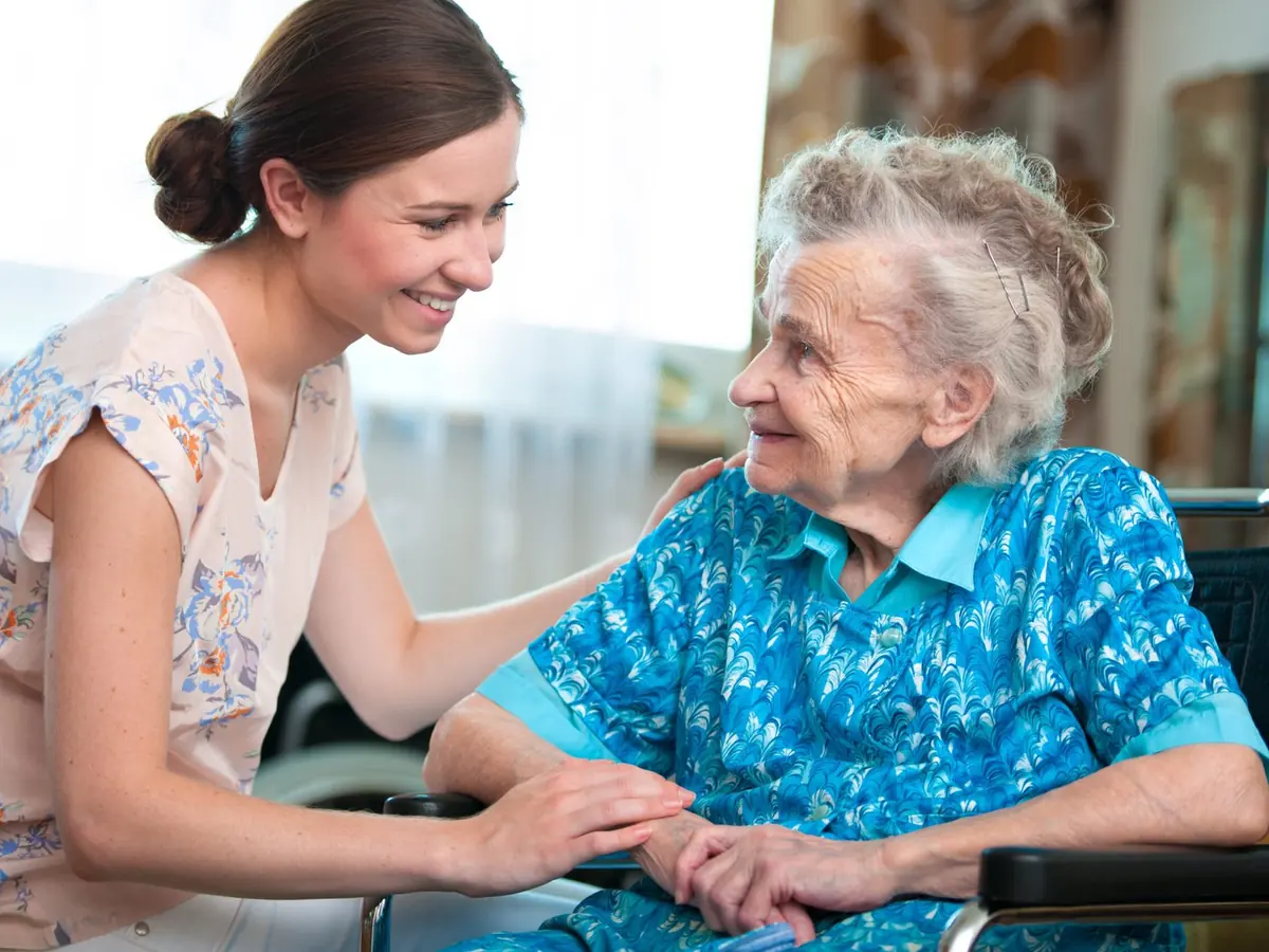 A carer holding hands and smiling with an older woman in a wheelchair