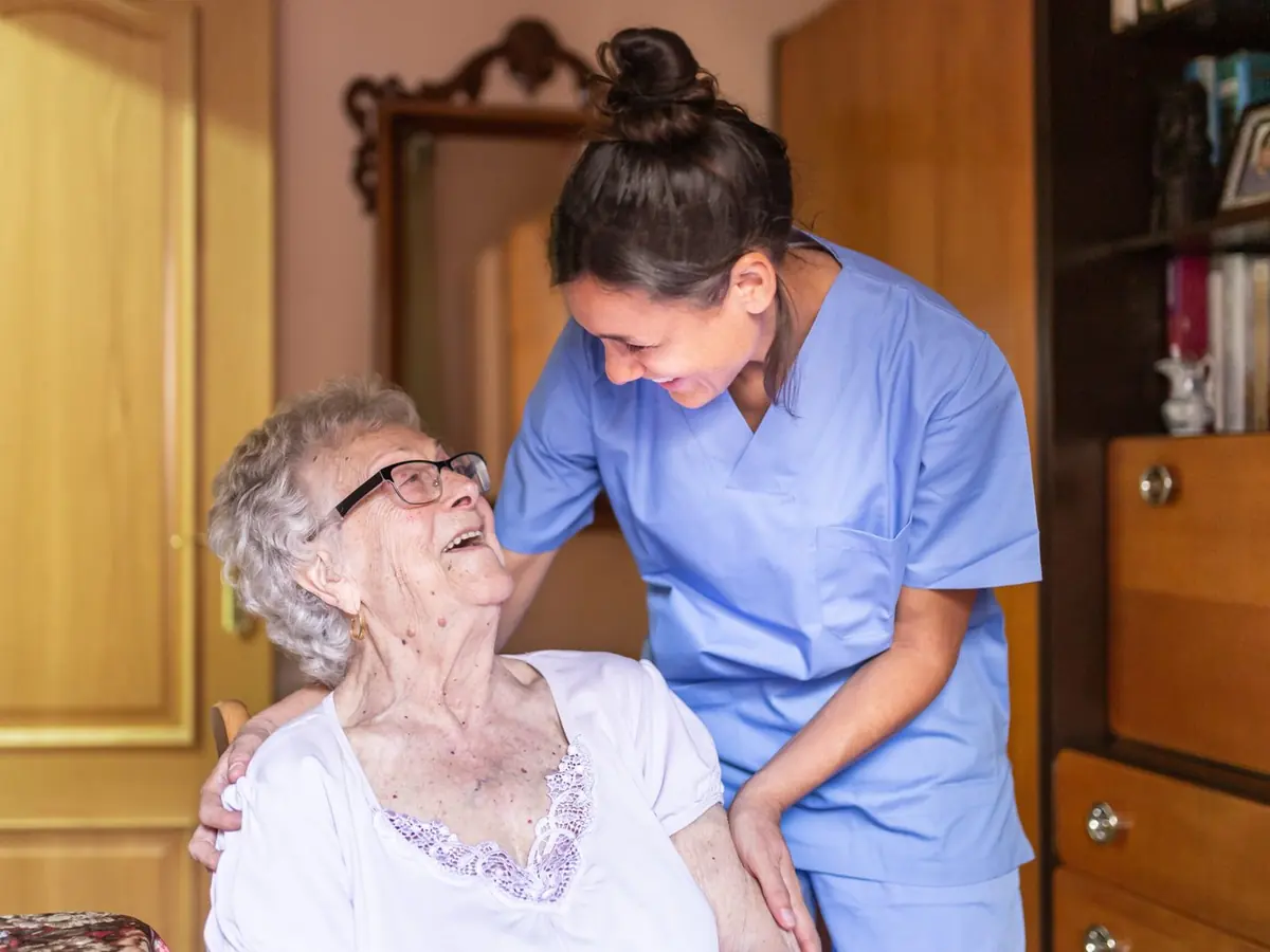 A smiling carer sharing a laugh with an older woman in her home